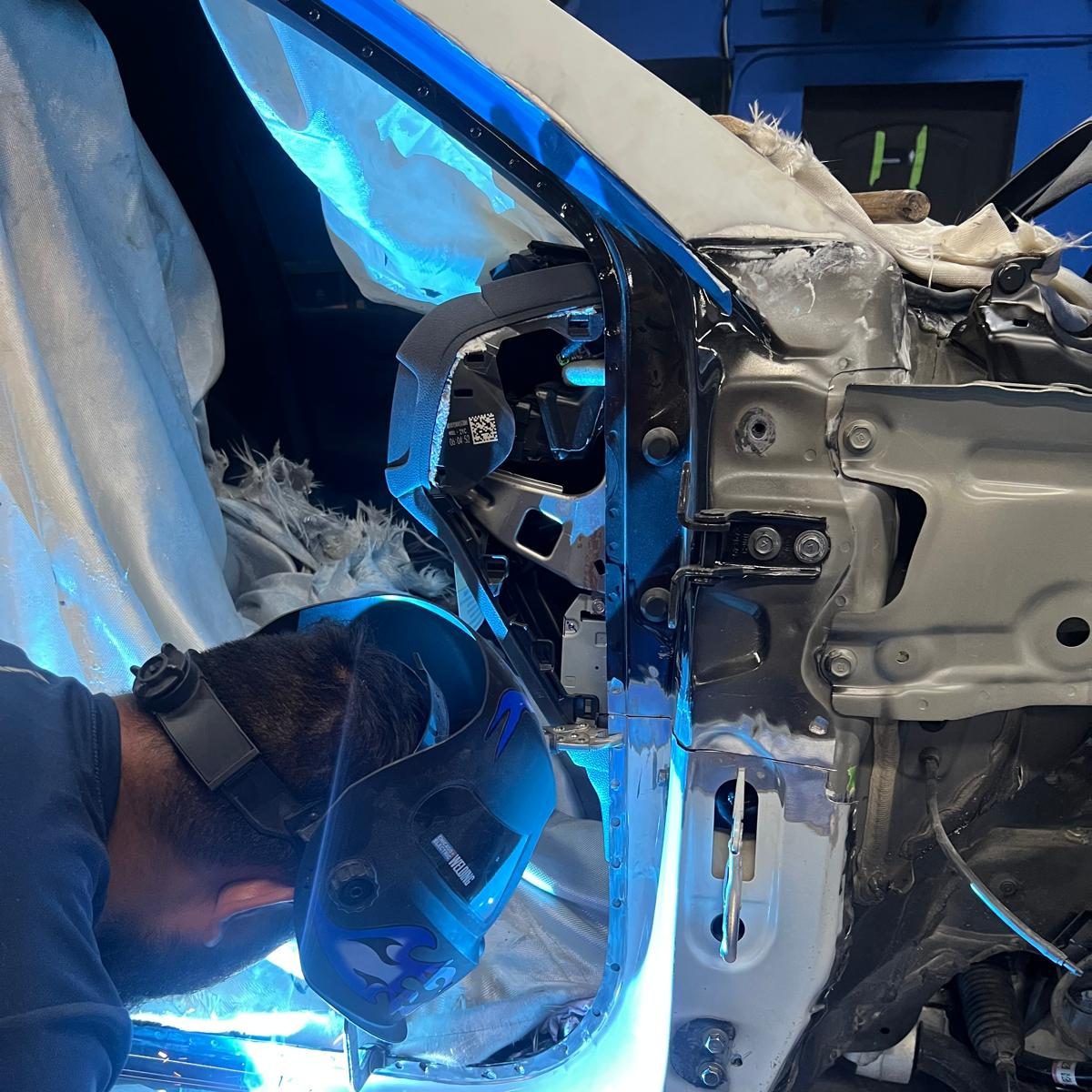 Technician in a welding mask performing structural welding on an A-pillar